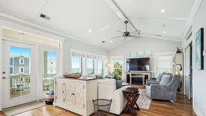 A spacious living area with a large TV, a ceiling fan, and a view of the outside. - Pier Walker: Spacious, Beautiful Home with Amazing Ocean Views Steps from OKI Pi (Oak Island)
