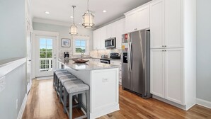 A modern kitchen with white cabinetry, stainless steel appliances, and a central island with bar stools. - Pier Walker: Spacious, Beautiful Home with Amazing Ocean Views Steps from OKI Pi (Oak Island)
