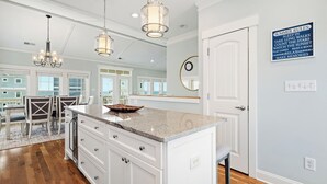 A spacious kitchen with a large island, pendant lighting, and a view to the dining area. - Pier Walker: Spacious, Beautiful Home with Amazing Ocean Views Steps from OKI Pi (Oak Island)