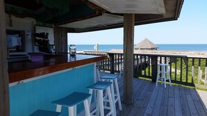 A wooden deck with a bar area, stools, and a view of the ocean. - BIS-Duck Resort - Spacious 2BR/2BA with Pool, Courtyard, Ocean View (Duck)
