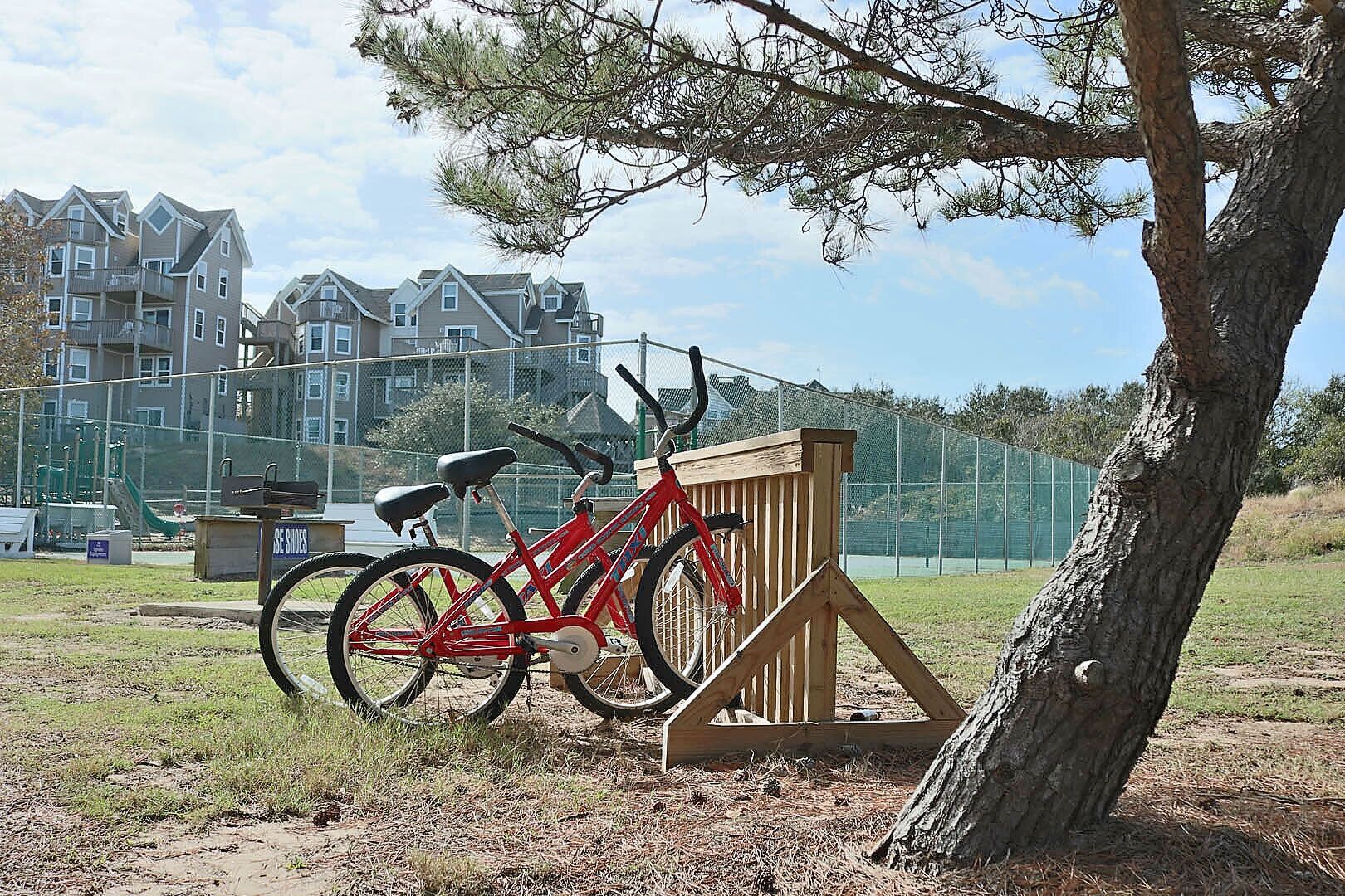 A red bicycle parked near a wooden structure in a grassy area with a playground and apartment buildings in the background.