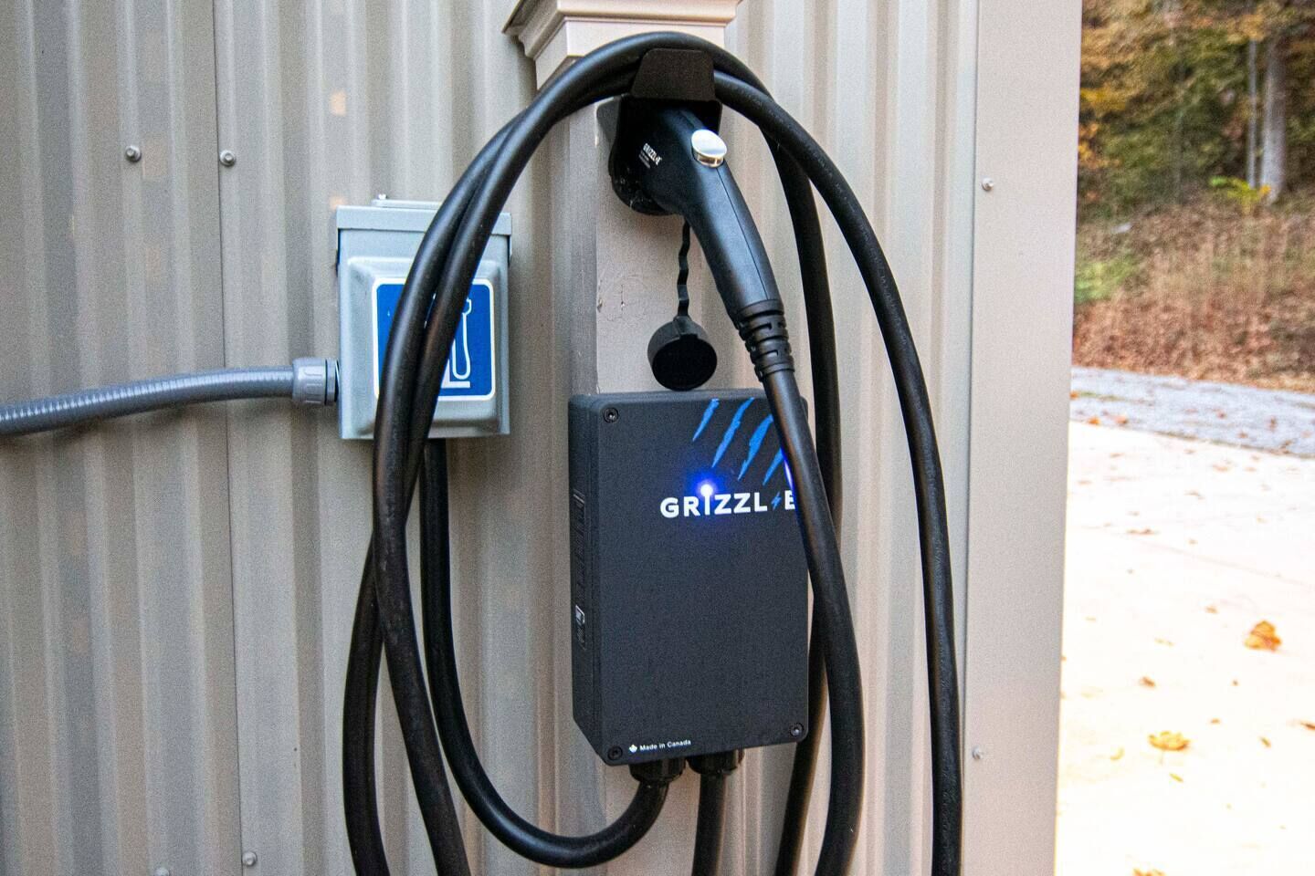 Een draagbare elektrische laadpaal met het merk 'GRIZZL E', bevestigd aan een golfplaten muur.