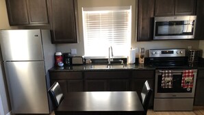 A modern kitchen with dark wood cabinets, stainless steel appliances, a black countertop, and a dining table with two chairs. - Riverside Cabin 5 - (Brand New Construction) (Grants Pass)