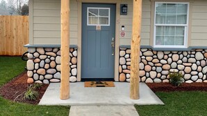 A house with a stone foundation, a blue front door, and a small porch with wooden posts. - Riverside Cabin 5 - (Brand New Construction) (Grants Pass)