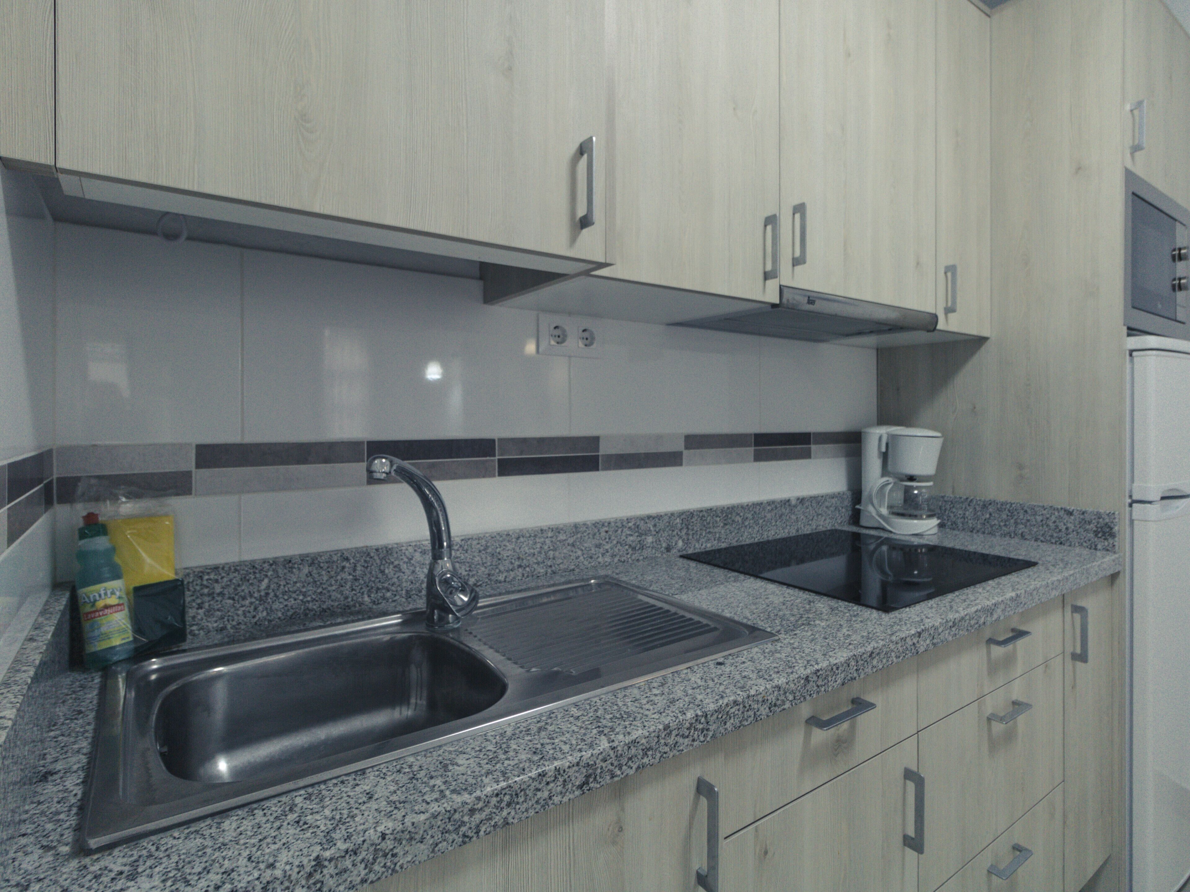 Eine Küche mit Granit Arbeitsplatten, Spüle aus Edelstahl und Holzschränken.