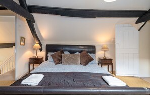 Ein Schlafzimmer mit einem großen Bett, zwei Nachttischen inklusive Lampen, einer weißen Tür und einer Treppe.
