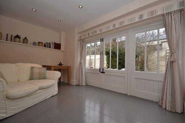A spacious room with a white sofa, a wooden side table, and a large window with curtains.
