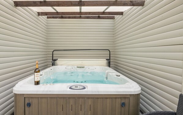 A hot tub with a wooden base, a control panel, and a bottle of wine.