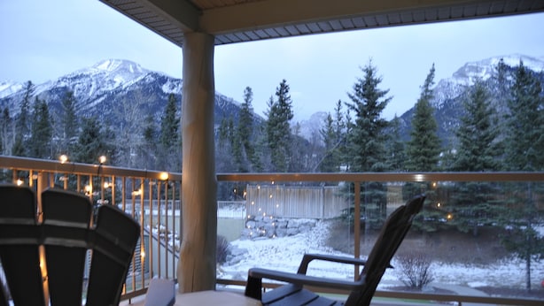Un balcone con sedie e tavolo che si affaccia su un paesaggio innevato con montagne e alberi.