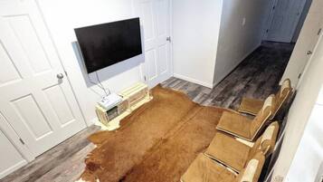 A room with a large brown rug, white walls, a mounted TV, and a wooden bench with cushions.