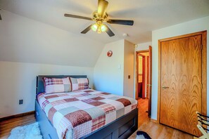 A bedroom with a bed, a ceiling fan, a wooden door, and a small picture on the wall.