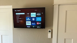 A flat-screen TV mounted on a textured wall, displaying a Roku TV interface with various streaming options. - Riverside Cabin 6 (Grants Pass)