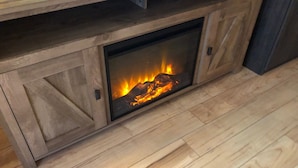 A fireplace with a fire burning inside, set in a wooden cabinet with a wooden floor. - Riverside Cabin 6 (Grants Pass)