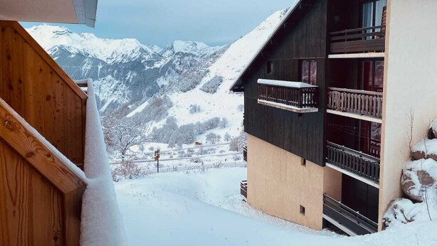 Ein Holzhaus mit Balkon vor verschneiten Bergen.