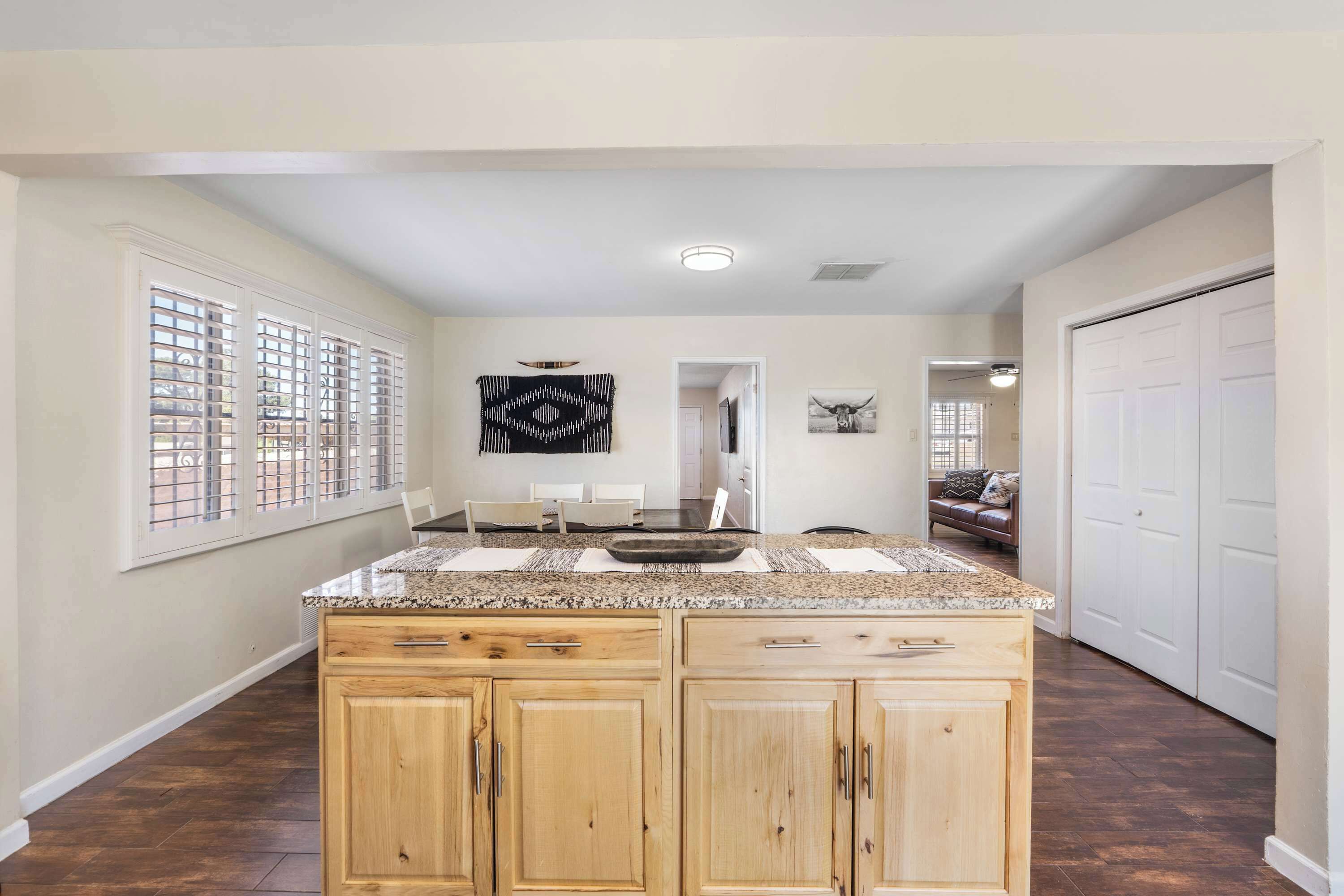 A kitchen with wooden cabinets, a granite countertop, and a window with blinds.