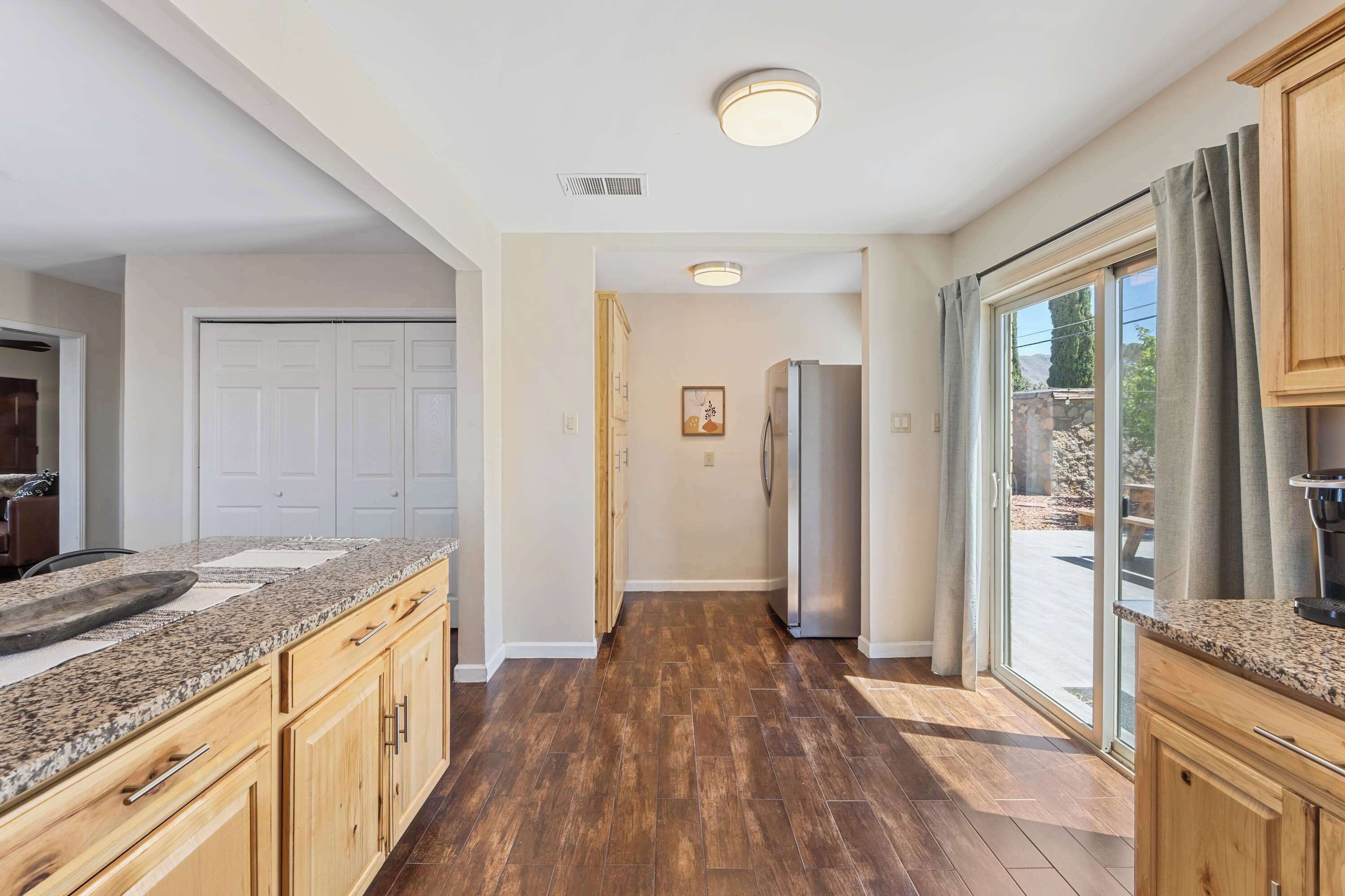 A kitchen with granite countertops, wooden cabinets, a refrigerator, and a sliding glass door leading to an outdoor area.