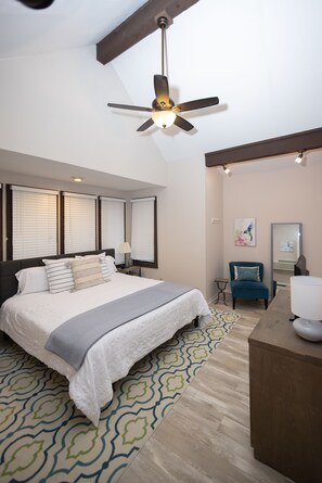 A bedroom with a large bed, a ceiling fan, a desk, and a chair.