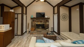 A living room with a fireplace, a sofa set, a television, and a kitchen area with a microwave. - Pool Side Getaway With Hot Tub at Tan-Tar-A Estates! Bordering Margaritaville! (Osage Beach)