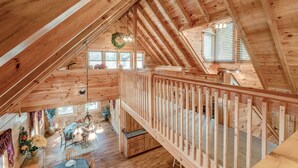 Una cabaña de madera con un dormitorio en el altillo, un comedor y una escalera.