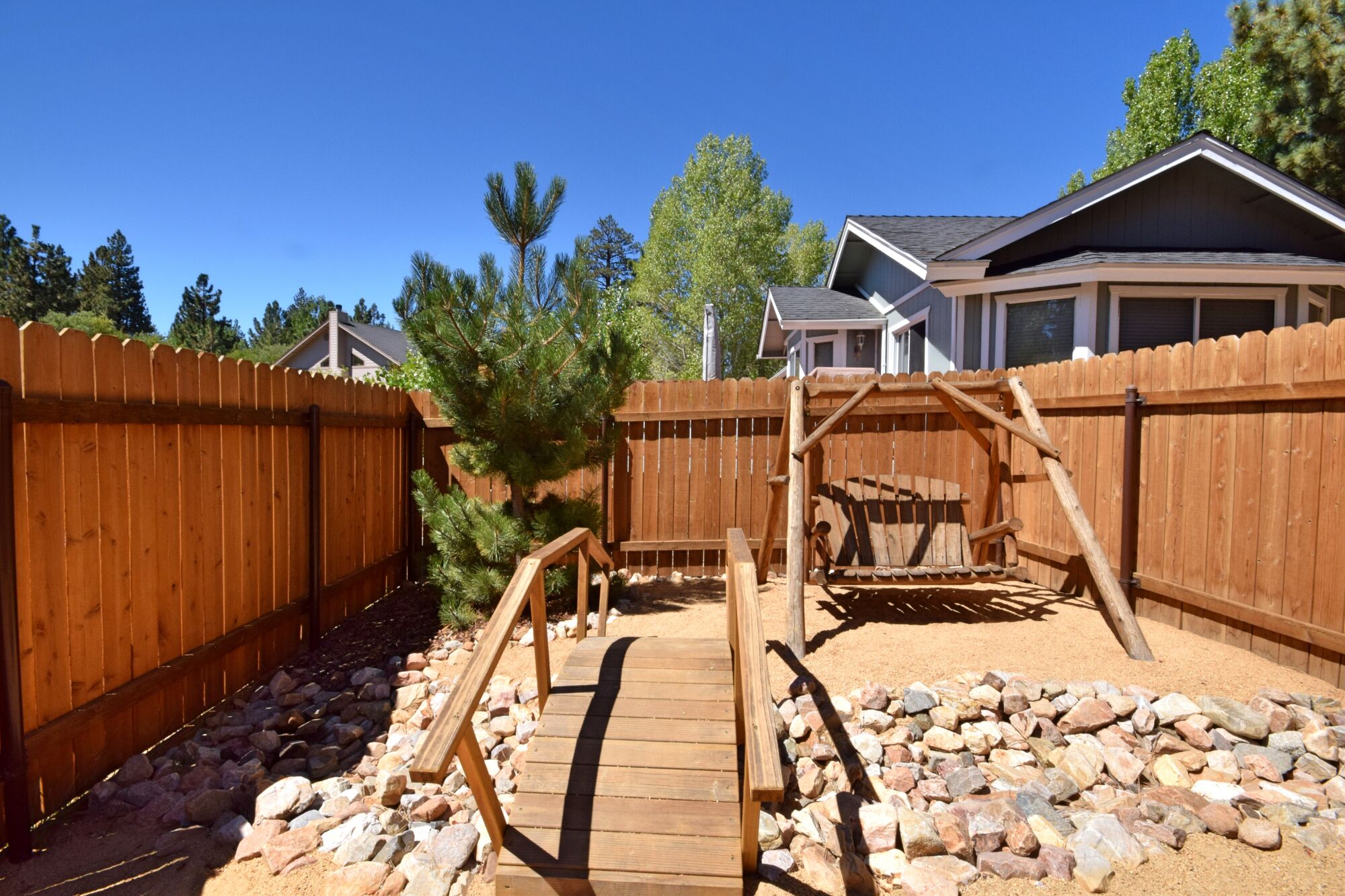 A wooden play structure with a bridge in a backyard.