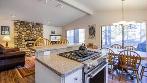 Une cuisine dotée d’un plan de travail en granit, d’une cuisinière à gaz et d’un coin repas avec des chaises et une table en bois.