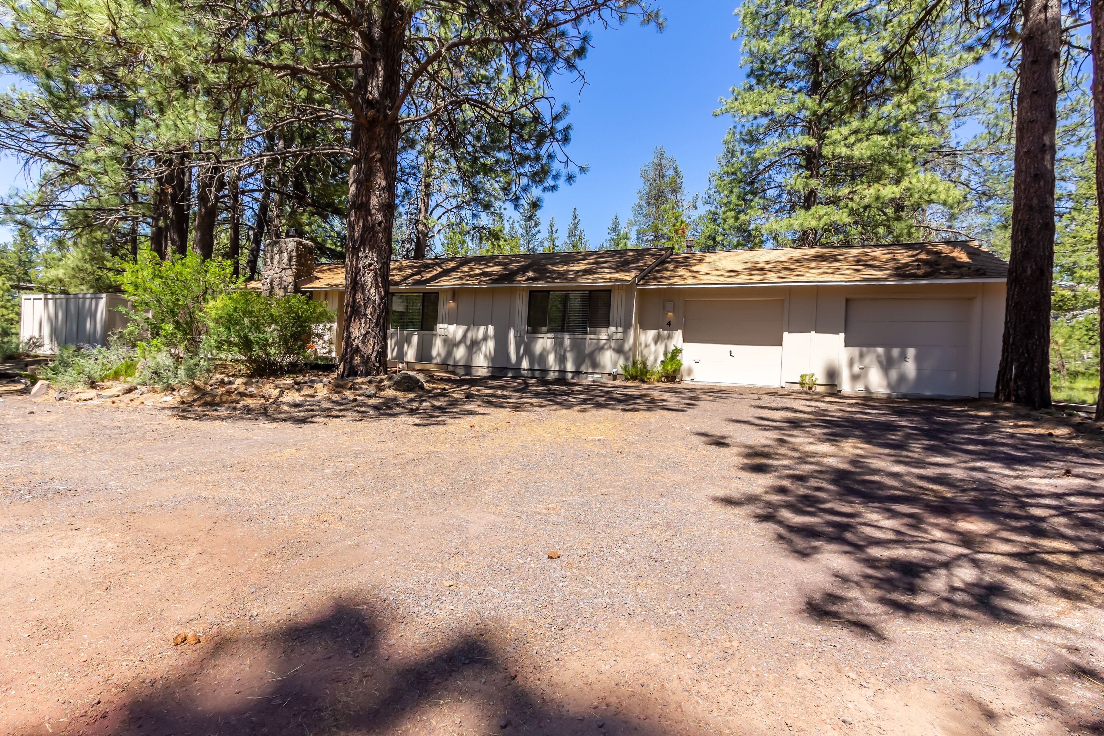 A single-story house with a garage, surrounded by trees and a gravel driveway.