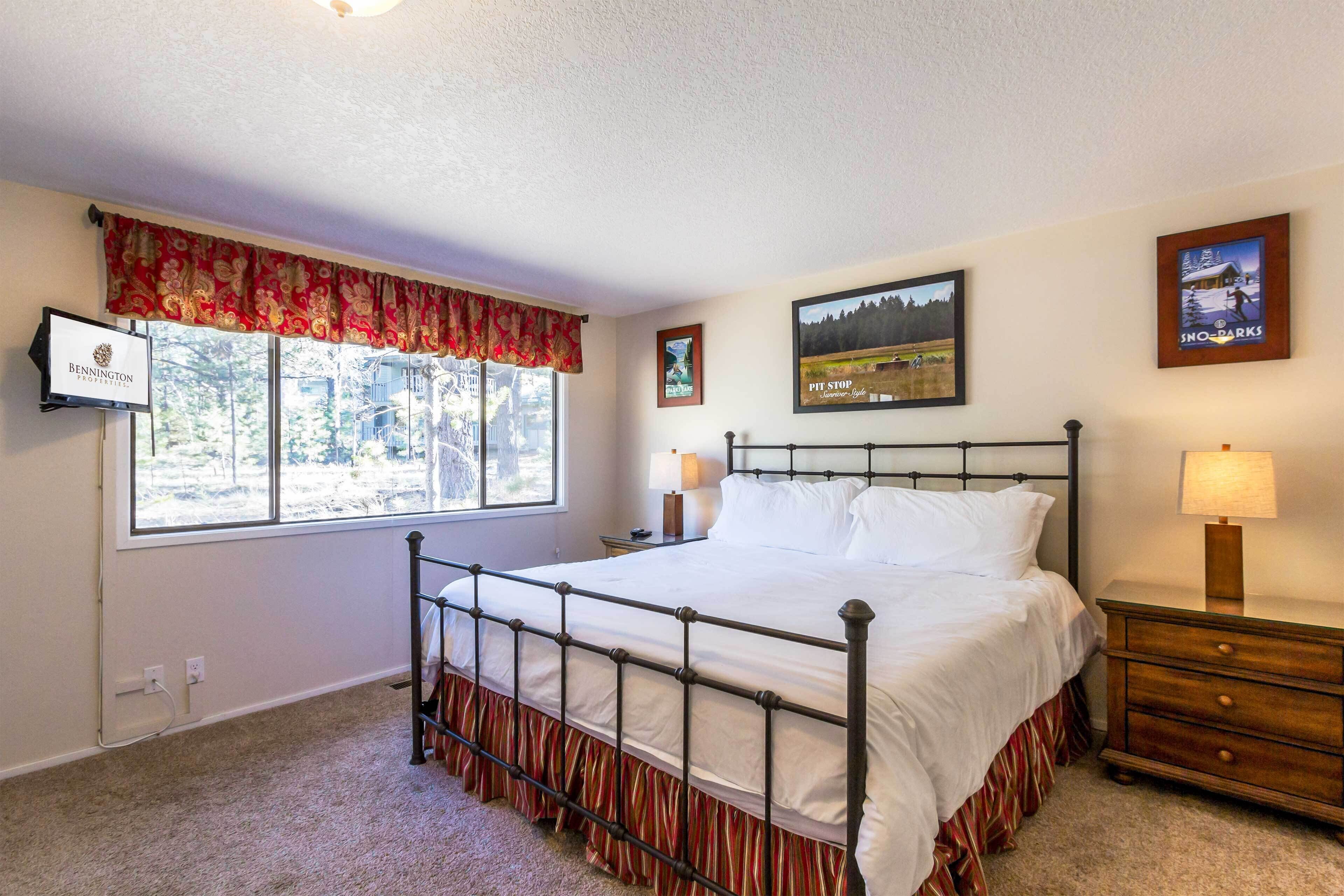 Een slaapkamer met een hemelbed, een raam met uitzicht op het landschap, een televisie aan de muur en een ingelijst beeld van een besneeerd landschap.