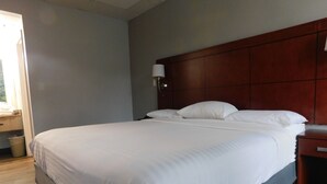 A neatly made bed with white linens in a room with wooden headboard and a nightstand.