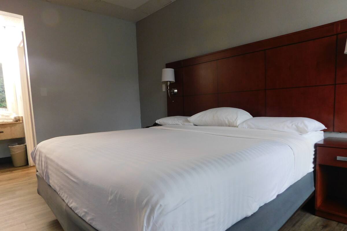 A neatly made bed with white linens in a room with wooden headboard and a nightstand.