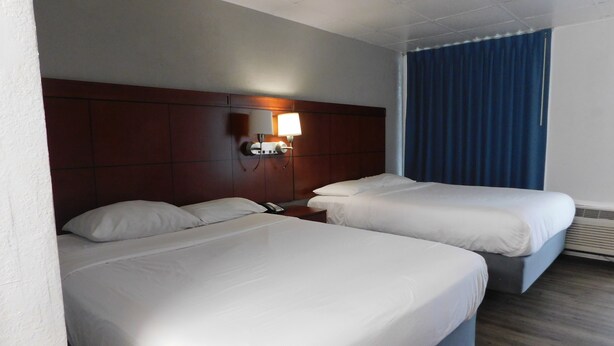 A hotel room with two beds, a wooden headboard, a nightstand, a lamp, and a window with curtains. - Park View Inn (Greensboro)