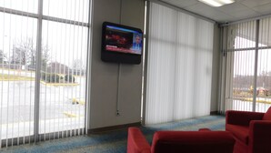 A conference room with a large window, a flat-screen TV mounted on the wall, and red chairs. - Park View Inn (Greensboro)