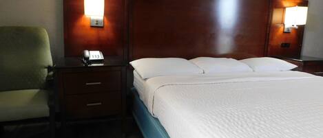 A hotel room with a bed, a desk with a telephone, and two wall-mounted lamps.