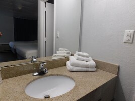 Un baño con lavamanos, espejo y toallas apiladas.
