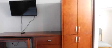 Une pièce comprenant un bureau en bois, un téléviseur fixé au mur et une grande armoire en bois à deux portes.
