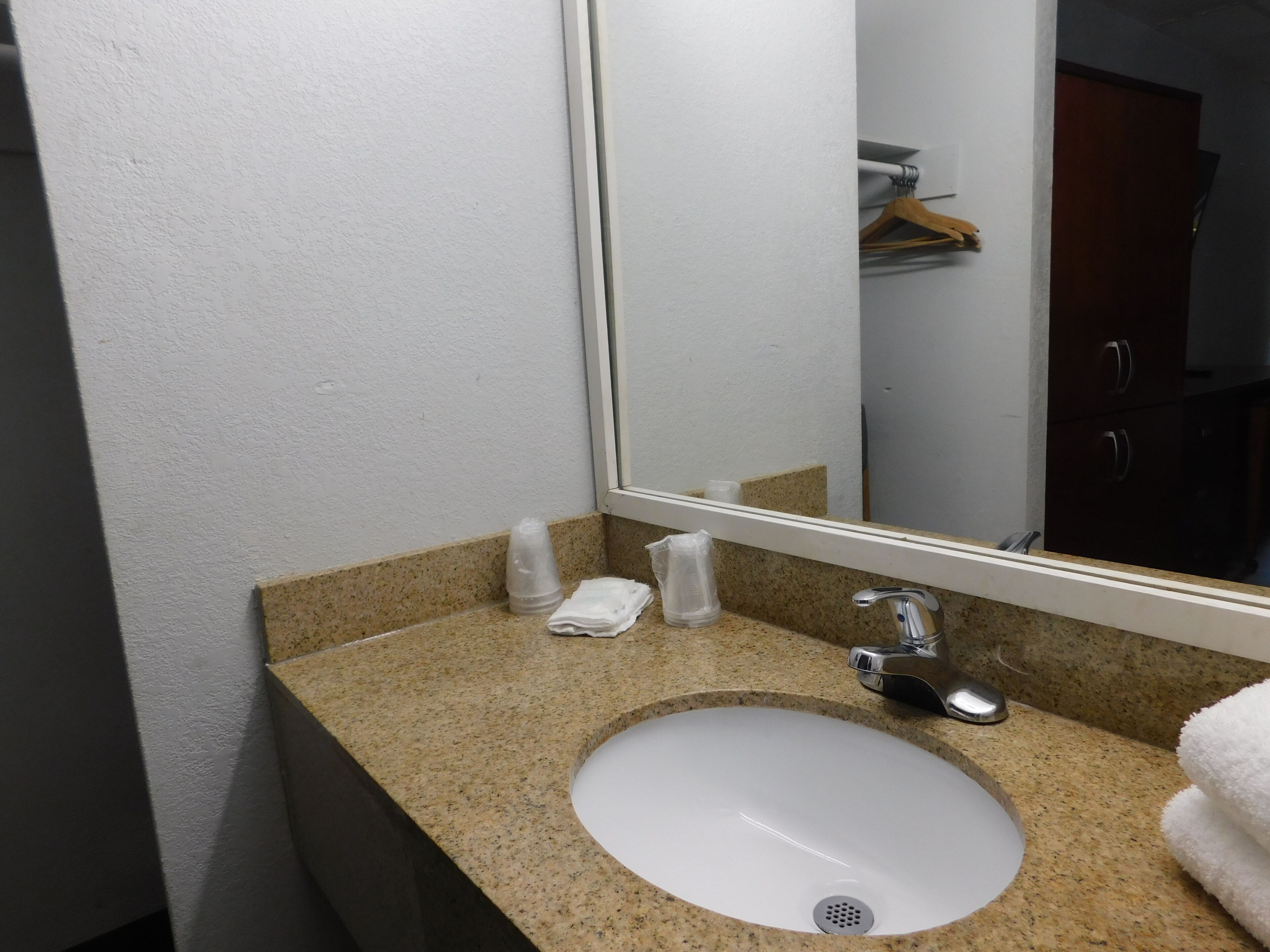 Un baño con encimera de granito, lavabo blanco, espejo y toallero.