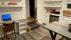 A modern kitchen with white cabinetry, a wooden dining table, and a laptop on a white countertop.