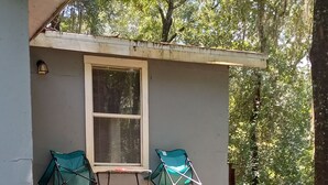Eine kleine Holzhütte mit einer Holztreppe, die zu einer Veranda führt. Auf der Veranda stehen zwei grüne Klappstühle.