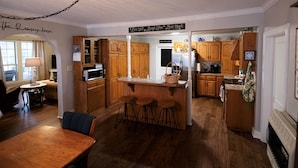 Una cocina con gabinetes de madera, una isla central con taburetes, un refrigerador y un microondas.