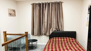 Un dormitori amb un llit, una finestra amb cortines, una escala i una taula rodona petita.