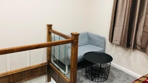 Habitació amb escala de fusta, barana de vidre, sofà blau, taula rodona negra i paret amb un rètol decoratiu.