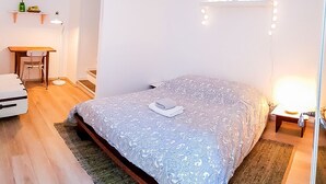 A bedroom with a bed, bedside table, lamp, and a small desk with a chair. - Cosy apartment for 1 to 4 people near the CHU (Rouen)