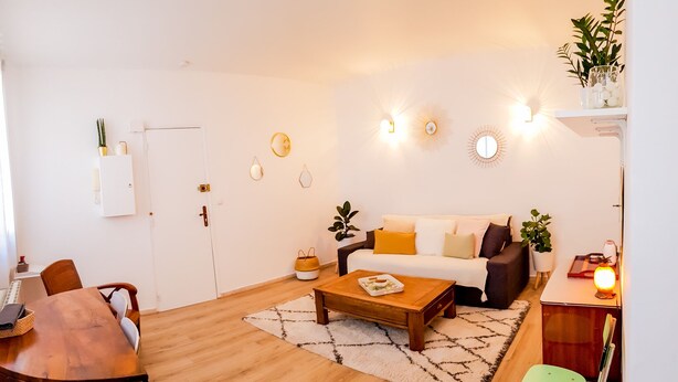 A living room with a wooden coffee table, a sofa with cushions, a dining table with chairs, and a small side table with a lamp. - Cosy apartment for 1 to 4 people near the CHU (Rouen)