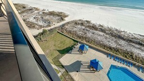 Uma área de piscina com espreguiçadeiras e guarda-sóis, vista para a praia e um caminho de areia que leva até a praia.