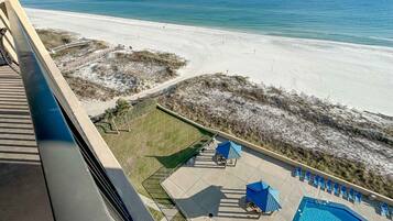 Ein Poolbereich mit Liegestühlen und Sonnenschirmen, Blick auf den Strand und ein Sandweg zum Strand.