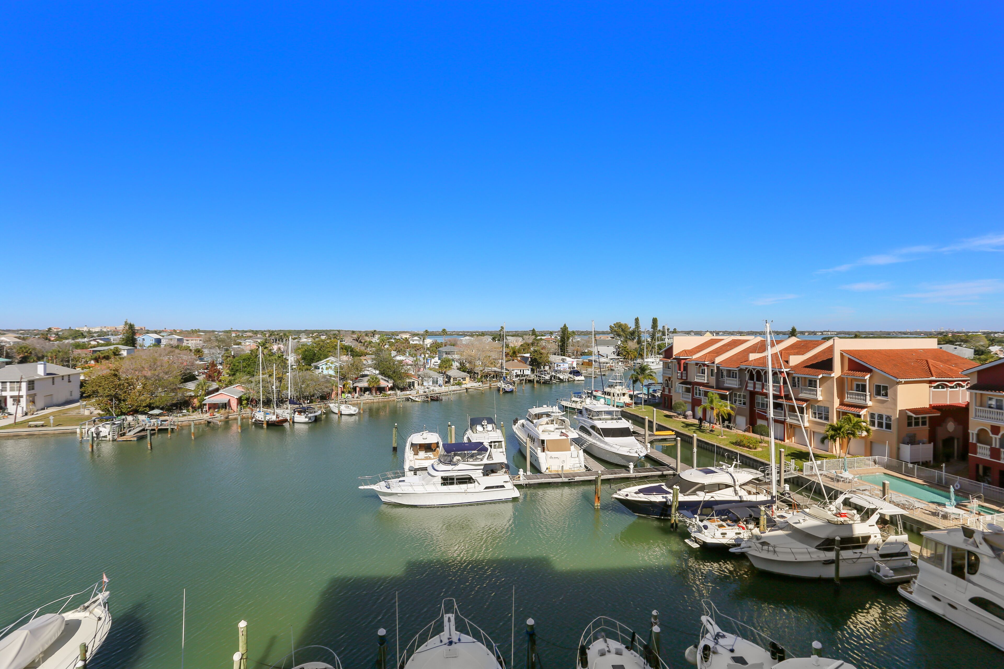 A marina with various boats docked, surrounded by buildings and a clear blue sky.