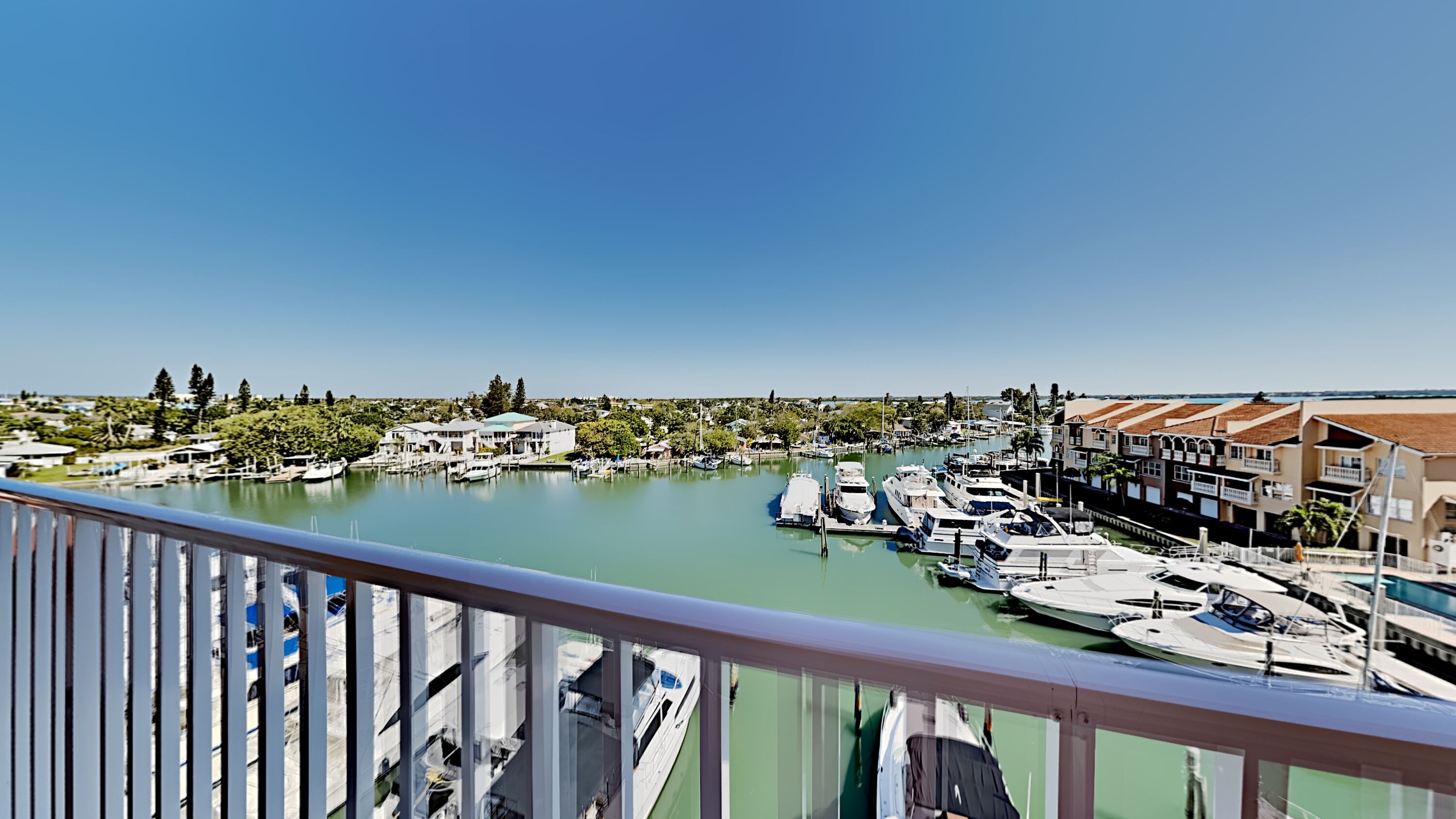A marina with boats docked, a clear sky, and residential buildings in the background.