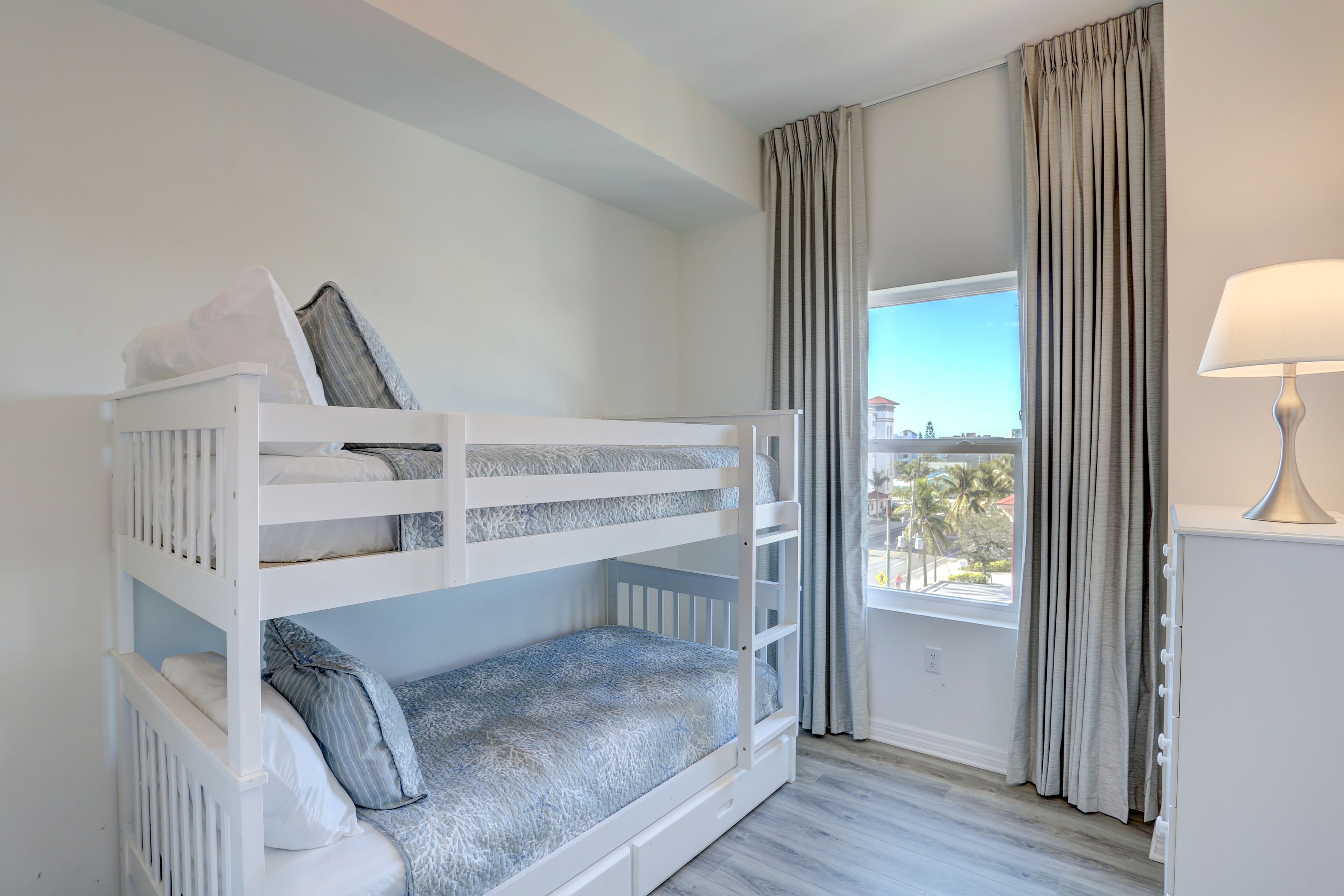 A bunk bed room with a window and curtains, a lamp, and a view of the outside.