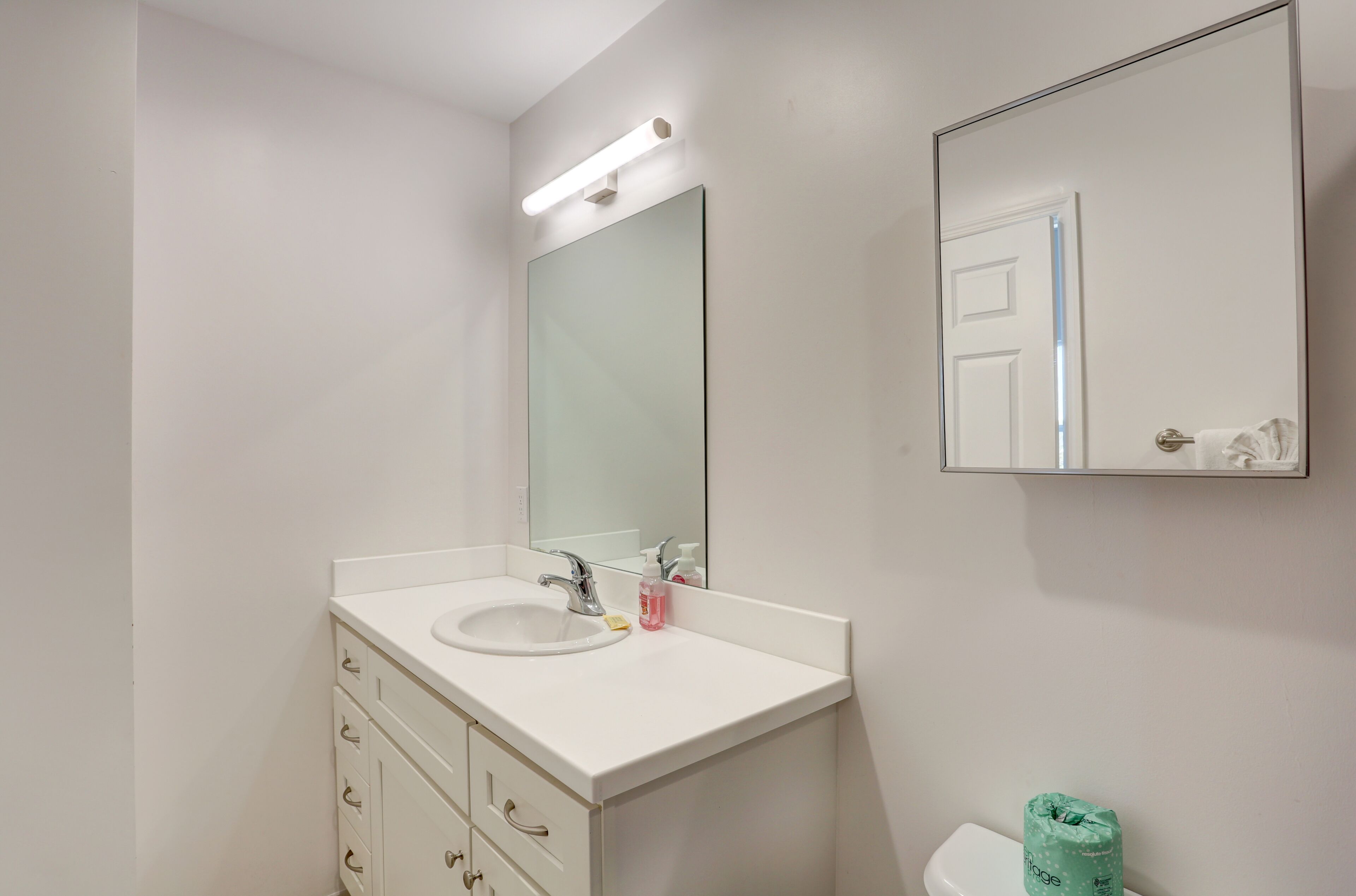 Un baño con lavamanos blanco, espejo e inodoro.