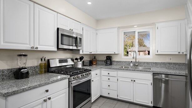 A modern kitchen with white cabinets, stainless steel appliances, granite countertops, and a window with a view of the outside. - Hidden Gem Upgraded 4/2 in NW Fresno w RV Parking (Fresno)