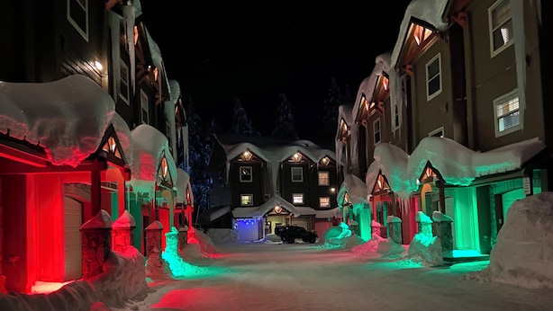 Een sneeuwbedekte straat met huizen verlicht door kleurrijke lampen.